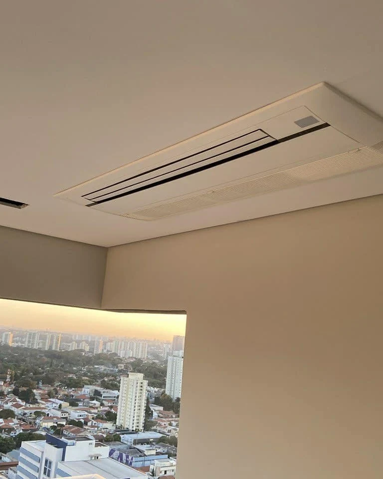 Evaporadora de duto embutida no forro de um apartamento alto, com a cidade ao fundo pela sacada